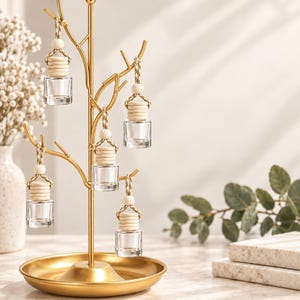 May include: A gold-colored metal tree-shaped stand with a circular base, featuring multiple branches. Five small, clear glass bottles with light-colored wooden caps and braided rope loops are suspended from the branches of the metal tree stand.