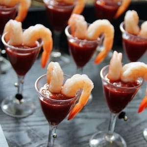 May include: A tray of shrimp cocktail appetisers. Each glass contains a red cocktail sauce and two prawns.