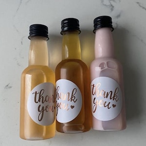May include: Three small glass bottles with black lids and white labels. The labels have a gold cursive font that says "thank you" with a small heart. The bottles contain different colored liquids.