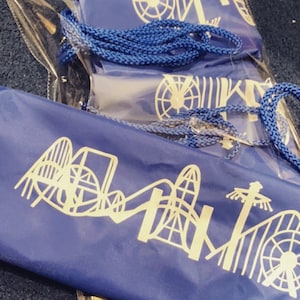 May include: Three blue fabric bags with white outlines of a roller coaster and Ferris wheel. The bags have drawstrings and are packaged in a clear plastic bag.