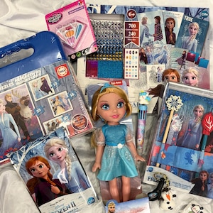 May include: A collection of Frozen II themed toys and crafts, including a doll in a blue dress, puzzles, sticker sets, and a small snowman figurine. The items are packaged in various boxes and containers, with the Frozen II logo visible.