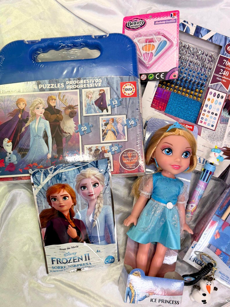 May include: A collection of Frozen II themed toys and accessories. Includes a doll in a blue dress, a puzzle, a beauty kit, and various craft supplies. The items are arranged on a white surface.