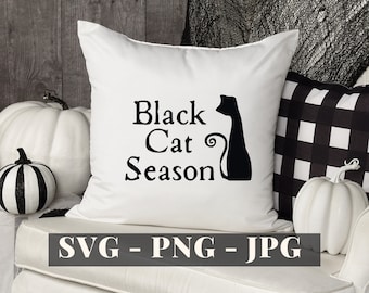 Pode incluir: Travesseiro branco com texto preto que diz "Black Cat Season" e uma silhueta preta de um gato sentado com o rabo enrolado. O travesseiro está em um sofá branco com um travesseiro xadrez preto e branco e uma abóbora branca.