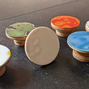 May include: Five round ceramic knobs with abstract patterns in various colors, including blue, green, orange, and white, mounted on wooden bases.