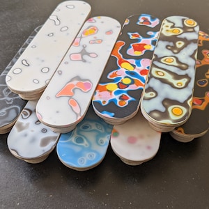 May include: A set of eight wooden coasters featuring abstract, colourful patterns. The coasters are oval-shaped and have a smooth, polished finish.