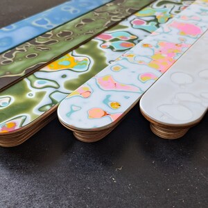 May include: Six wooden strips with rounded ends, each featuring a different abstract pattern in shades of blue, green, pink, yellow, white, and orange.