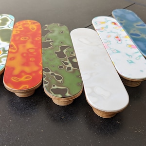 May include: Six colourful, oval-shaped cabinet knobs with a marbled design. The knobs are made of wood and have a light brown finish.