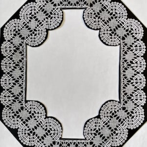 May include: A white lace doily with a black octagonal frame. The lace is intricate and delicate, with a repeating pattern of small circles and loops.