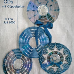 May include: Four blue and white crocheted CDs with blue ribbon accents. The CDs are hanging from the ceiling. The text "CDs mit Klöppelspitze" and "© khn. Juli 2006" is visible in the image.