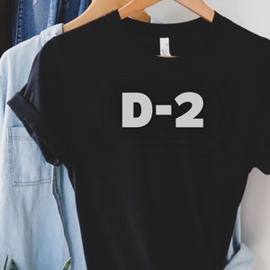 Peut inclure: T-shirt noir avec du texte blanc qui dit "D-2".