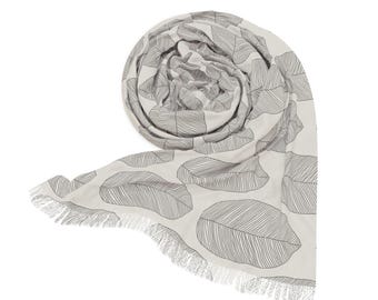 May include: A rolled-up, off-white scarf with a repeating pattern of large, gray leaf outlines. The scarf has a fringed edge. The design is simple and elegant, suitable for various styles.