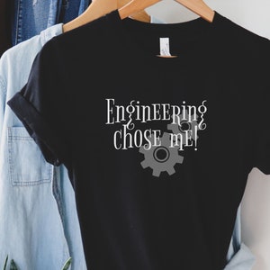 May include: Black t-shirt with white text that reads "Engineering chose me!" and a gray gear graphic.