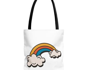 May include: White tote bag with a black handle. The bag features a cartoon rainbow design with orange, red, and blue arches, and two smiling cloud accents. Ideal for carrying items.