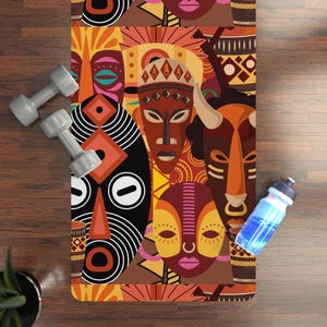 May include: A yoga mat with a colorful pattern of African masks. The masks are in shades of brown, orange, yellow, red, and black. The mat is perfect for yoga, pilates, or stretching.