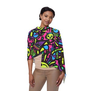 May include: A vibrant, colorful shawl featuring a neon pink background with a black outline and abstract shapes in blue, green, and purple. The shawl has a fringed edge and is draped over the shoulders.