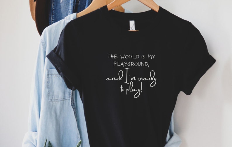 Op de afbeelding: Zwart T-shirt met witte tekst die luidt: "De wereld is mijn speeltuin, en ik ben klaar om te spelen!"