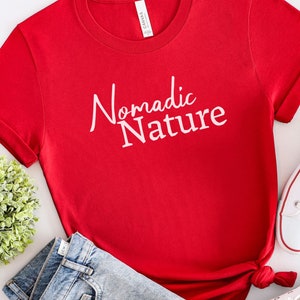 May include: Red short-sleeved t-shirt with white text that reads "Nomadic Nature".