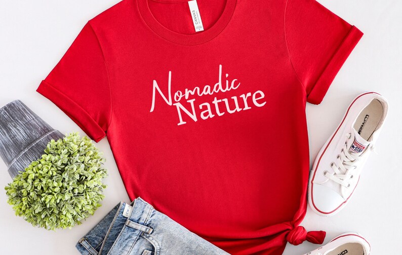 May include: Red short-sleeved t-shirt with white text that reads "Nomadic Nature".