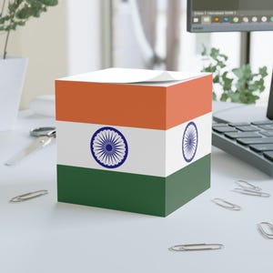 May include: A cube-shaped notepad featuring the Indian flag design. The top section is orange, the middle is white with a blue wheel emblem, and the bottom is green. The notepad is on a white surface with paper clips and office supplies.