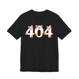 May include: Black t-shirt featuring the number 404 in white and orange. The design incorporates cat faces within the numbers, giving a playful and unique look. The shirt is made of a soft material.