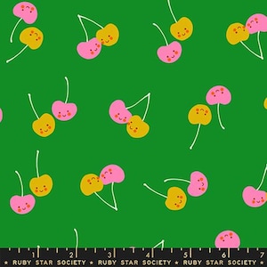 May include: A green fabric featuring a repeating pattern of pairs of cherries with smiling faces in pink and mustard yellow. Each cherry has a thin white stem. A black ruler at the bottom shows measurements in centimetres from 0 to 18 centimetres.