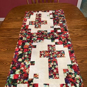 May include: A white table runner with a floral pattern. The runner is made of fabric squares with a white background and a floral print. The runner is approximately 16 inches wide and 60 inches long.
