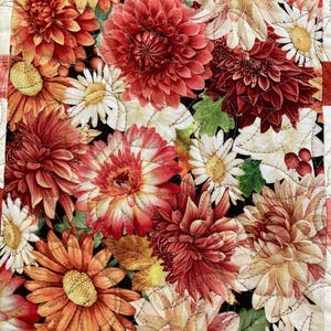 以下が含まれることがあります： 赤、オレンジ、クリーム色のダリアとデイジーが黒い背景に描かれた、花のキルトのクローズアップ。キルトは白い糸で縫い付けられており、テクスチャ効果を生み出しています。テキスタイルアートの美しい例です。