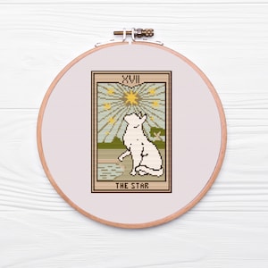 May include: A white cat sits on a green hill, looking up at a yellow star with rays of light. The card is labeled "XVIII THE STAR" in a brown frame.