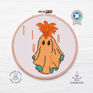 May include: Cross-stitch embroidery in a wooden hoop. The design features a cartoon ghost with orange hair and teal accents, with the word "TLAOS" stitched above. The design is labelled "Human Made" and "Tested". A "File Download" icon is also present.