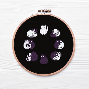 May include: A black embroidery hoop with a white background and a circle of black and white cats in different poses. The cats are all facing inwards towards the center of the circle.