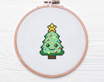 May include: A cross-stitch embroidery hoop with a green Christmas tree design. The tree has a yellow star on top and colorful lights. The tree has a smiling face with two black eyes. The text "50% OF PROCEEDS DONATED TO LOCAL CAT RESCUE!" is below the hoop.