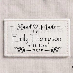 May include: A white rectangular label with black text that reads "Hand Made by Emily Thompson with love." The label has a stitched border and decorative leaf and heart accents. The number "3" is in the bottom right corner.