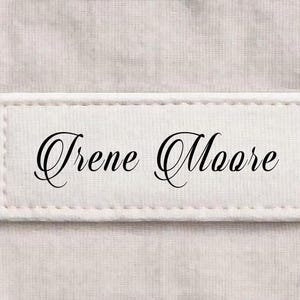 以下が含まれることがあります： エレガントな黒い筆記体で「Irene Moore」という名前が書かれた長方形の白い布ラベル。ラベルの縁は白い糸で縫われています。数字の「51」が右下に黒で表示されています。