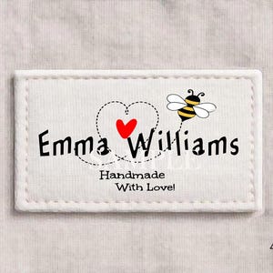 以下が含まれることがあります： 黒文字で「Emma Williams」と書かれた白い長方形のラベル。赤いハートと漫画のミツバチが描かれています。ラベルには「Handmade With Love!」の文字も含まれています。