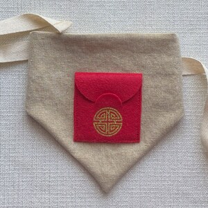 Pu&ograve; includere: Una piccola borsa in feltro rosso con un simbolo dorato sul davanti, all'interno di una borsa in tessuto beige pi&ugrave; grande con una tracolla bianca.