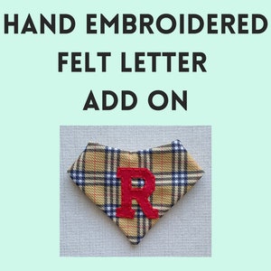 May include: A red felt letter "R" is hand-embroidered onto a yellow and black plaid fabric bandana. The bandana is folded in a triangle shape.