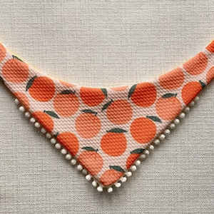 May include: A pink and orange bandana with a white pom-pom trim and a pattern of orange slices.
