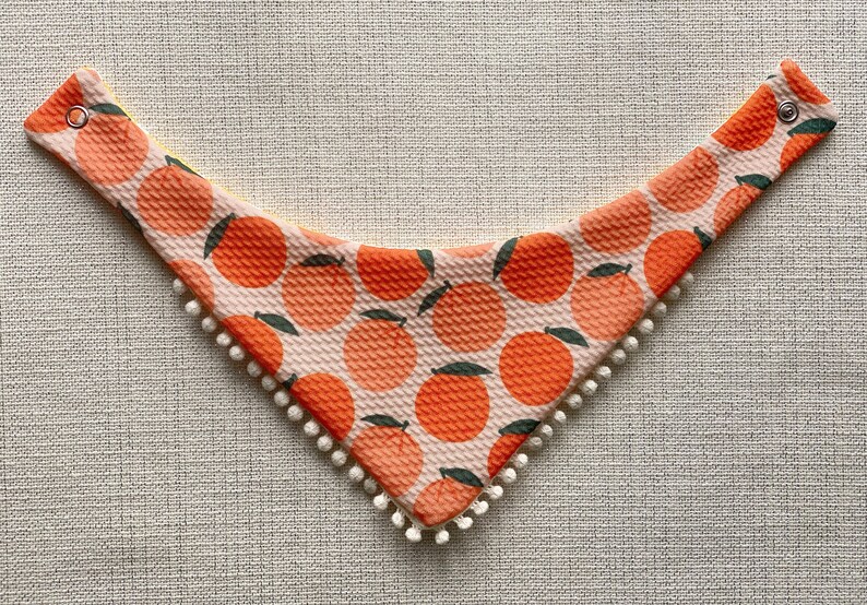 May include: A pink and orange bandana with a white pom-pom trim and a pattern of orange slices.
