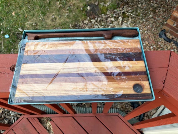 A matching set of a striped wood cutting board AND a hand-forged bow knife, both made in Montana — a complete, rustic, craftsman gift duo.