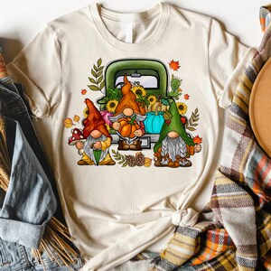 May include: Three gnomes in a green truck with a bed full of pumpkins, sunflowers, and fall foliage. The gnomes are wearing red, orange, and green hats.