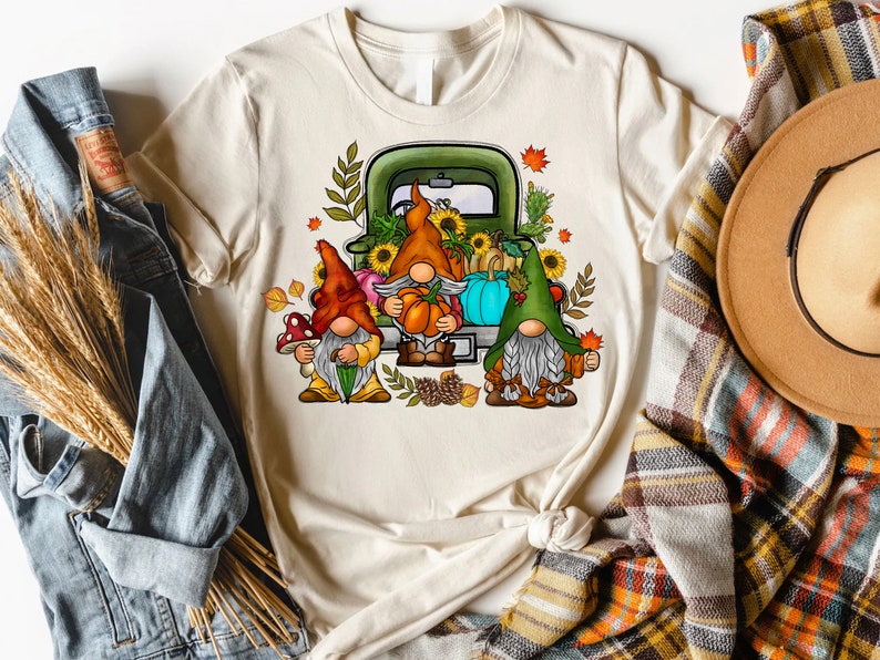 May include: Three gnomes in a green truck with a bed full of pumpkins, sunflowers, and fall foliage. The gnomes are wearing red, orange, and green hats.