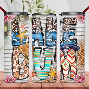 May include: Three stainless steel tumblers with a white background and colorful designs. The tumblers feature the words "LAKE BUM" with various patterns and images, including waves, starfish, and fishing poles.
