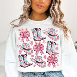 Peut inclure: Sweat-shirt blanc avec un motif de P&acirc;ques rose et bleu. Le motif repr&eacute;sente des bottes de cow-boy, des chapeaux, des n&oelig;uds et des oreilles de lapin.