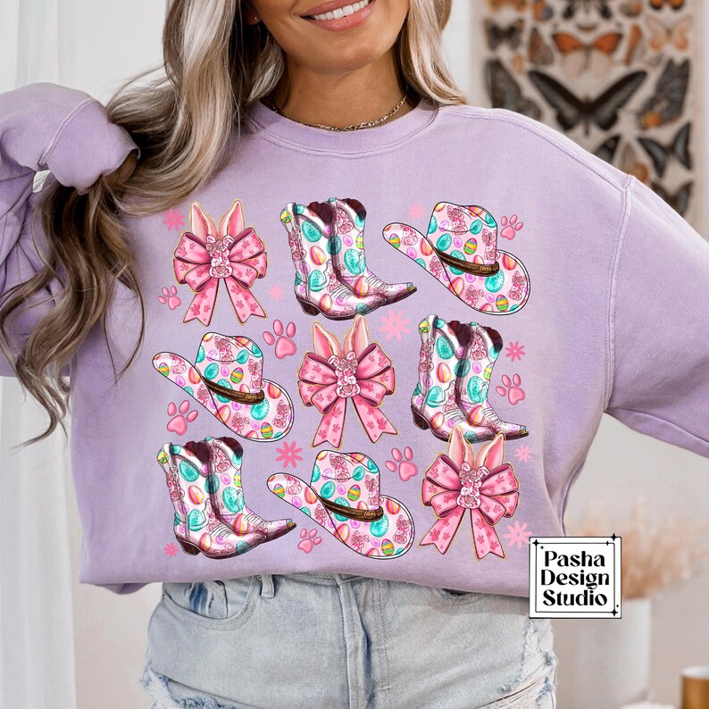 Peut inclure: Un sweat-shirt lavande avec un motif de P&acirc;ques color&eacute; comprenant des n&oelig;uds roses, des bottes de cow-boy et des chapeaux avec des &oelig;ufs de P&acirc;ques. Le motif est r&eacute;p&eacute;t&eacute; sur tout le sweat-shirt. Le texte "Pasha Design Studio" est visible dans le coin inf&eacute;rieur droit.