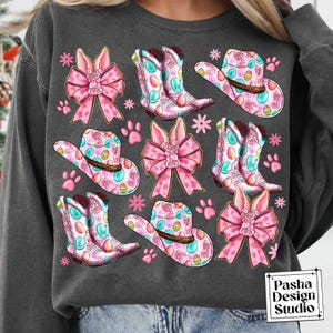 Peut inclure: Un sweat-shirt gris avec un motif de P&acirc;ques color&eacute;. Le motif pr&eacute;sente des n&oelig;uds roses, des bottes de cow-boy et des chapeaux de cow-boy avec des &oelig;ufs de P&acirc;ques. Le texte "Pasha Design Studio" est dans le coin inf&eacute;rieur droit.