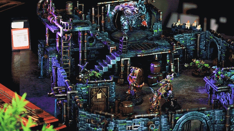 May include: A detailed miniature dungeon set with a green, blue and brown colour scheme. The set features a multi-level structure with stairs, a small door and a large, menacing figure at the top. There are several smaller figures throughout the set, including a figure holding a barrel.