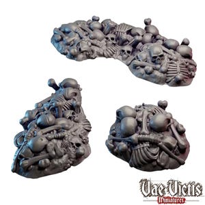 May include: Three grey miniature terrain pieces featuring piles of human skulls, rib cages, and various bones. The pieces are sculpted with detailed skeletal remains and include the text Vae Victis Miniatures in the bottom right corner.