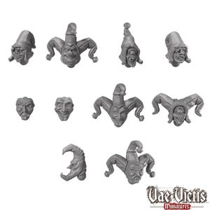 Peut inclure: Un ensemble de dix têtes miniatures en résine grise non peinte présentant divers designs inspirés des bouffons, incluant des personnages encapuchonnés, des masques et des figures à chapeaux pointus. Le texte Vae Victis Miniatures apparaît en bas à droite.
