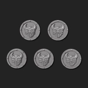 May include: Five grey, circular tokens featuring a horned helmet design. Each token has a raised border with small, evenly spaced dots. The background is a solid, dark grey.