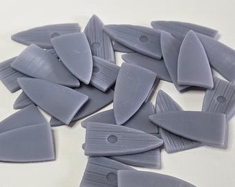 May include: A collection of small, grey, shield-shaped toggles. Each toggle features a pointed end, a flat base, and a single circular hole centered near the top. The surface of each piece displays a subtle, linear, wood-grain-like texture.